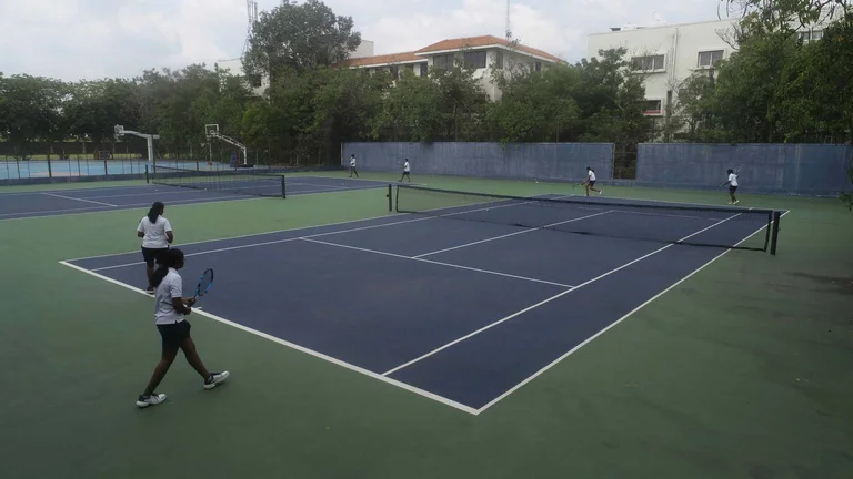 Students playing doubles tennis on outdoor courts at TIPS Erode CBSE campus, with basketball court visible in background