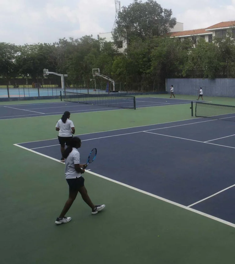 Students playing doubles tennis on outdoor courts at TIPS Erode CBSE campus, with basketball court visible in background